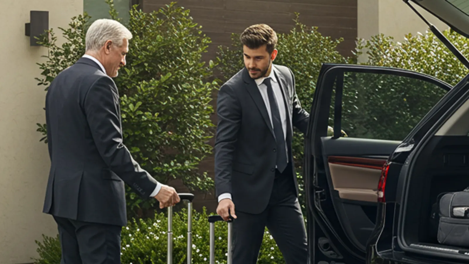 A uniformed chauffeur assisting an executive with luggage beside a black SUV for DFW corporate travel.